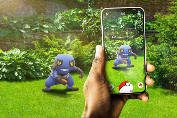 Imagem de uma pessoa jogando Pokémon GO em um jardim. O jardim possui plantas na cor verde e a pessoa está com um celular em sua mão esquerda apontando para um pokémon criado por Realidade aumentada no celular.