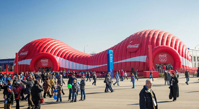 Imagem de um evento da Coca-cola. A imagem mostra uma grande estrutura na cor vermelha com logos da coca-cola