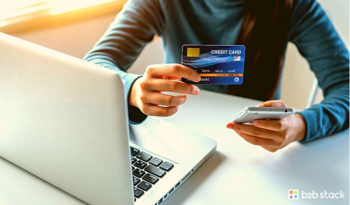 Imagem de uma pessoa com um cartão de crédito em suas mãos. A frente da pessoa a um notebook 