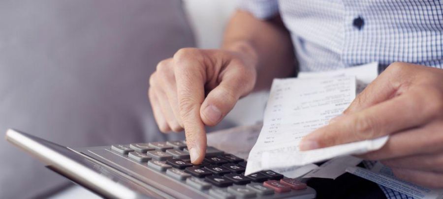 Imagem de um homem digitando em uma calculadora com uma nota fiscal na mão esquerda